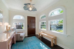 A room with a wooden door, a bench, a blue rug, and a ceiling fan.