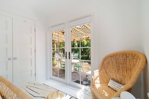 Una stanza con una porta bianca, una sedia in vimini con cuscino e vista su un patio esterno con tavolo e sedie.