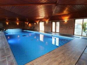 An indoor swimming pool with a wooden ceiling, brick walls, and a view of the outside through large windows. - Adelaide Cottage (Ashbourne)