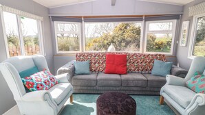 A cozy room with a grey sofa, two white armchairs, and a patterned cushion.