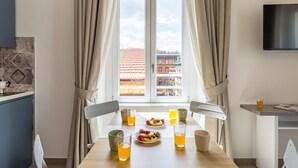Un comedor con una mesa preparada para dos personas, un televisor montado en la pared y una ventana con cortinas.