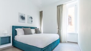 Un dormitorio moderno con una cama color turquesa, ropa de cama blanca y dos cuadros en la pared.