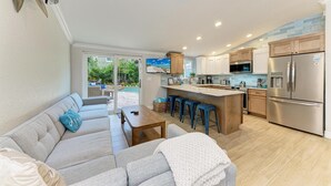A modern kitchen with a central island, stainless steel appliances, and a dining area with a sofa and bar stools. - Beach Bliss managed by Beach Retreats (Holmes Beach)