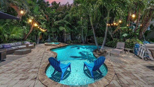 A pool area with blue chairs, a lounge area with sofas, and string lights. - Beach Bliss managed by Beach Retreats (Holmes Beach)