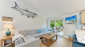 A modern living room with a grey sofa, a wooden coffee table, a fish wall art, a TV, and a view of the outdoors. - Beach Bliss managed by Beach Retreats (Holmes Beach)
