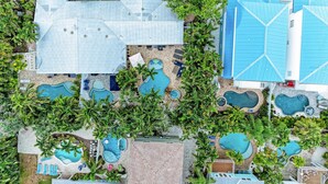 An aerial view of a resort with multiple swimming pools, palm trees, and a variety of building structures. - Beach Bliss managed by Beach Retreats (Holmes Beach)