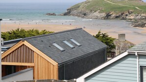 A coastal view with a beach, rocky cliffs, and a wooden building with a sloped roof. - 11 Ebbtide (Newquay)