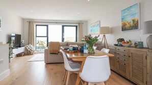 A modern living room with a sofa, dining table, chairs, and a TV. - 11 Ebbtide (Newquay)