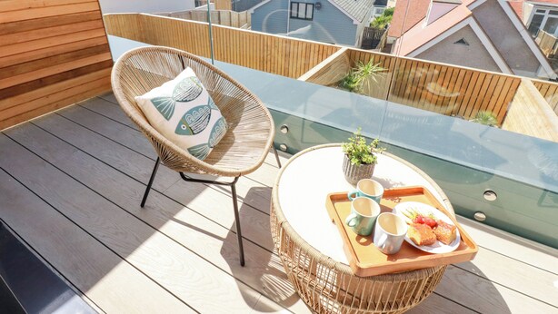 A balcony with wicker furniture, a glass table, and a tray with food and drinks. - 11 Ebbtide (Newquay)