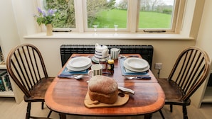 Una mesa de comedor con sillas, un radiador y una ventana con vistas a un jardín.