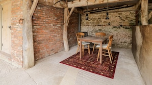 Una habitación rústica con paredes de ladrillo visto, vigas de madera, una mesa de madera con sillas y una alfombra estampada.