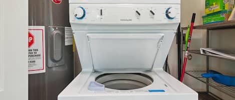 A front-loading washing machine with a control panel, a water heater, and a shelf with cleaning supplies.