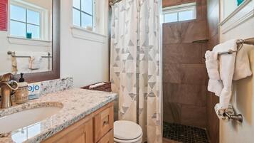 A bathroom with a marble sink, a toilet, a shower with a patterned curtain, and a towel rack.