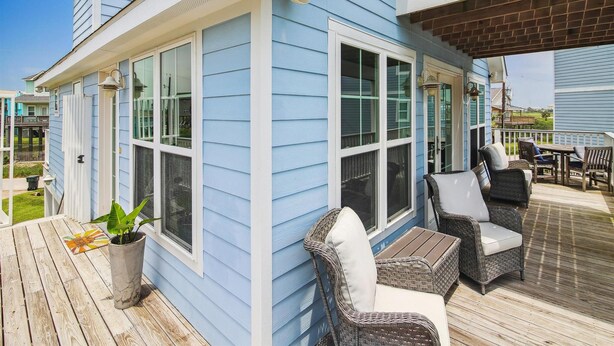 A two-story house with a covered deck, large windows, and outdoor furniture. - Beach Rays by Ryson Vacation Rentals (Galveston)
