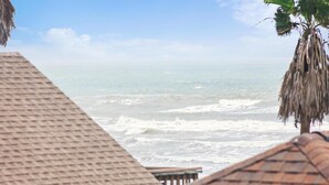 A beach view with a thatched roof structure in the foreground. - Beach Rays by Ryson Vacation Rentals (Galveston)