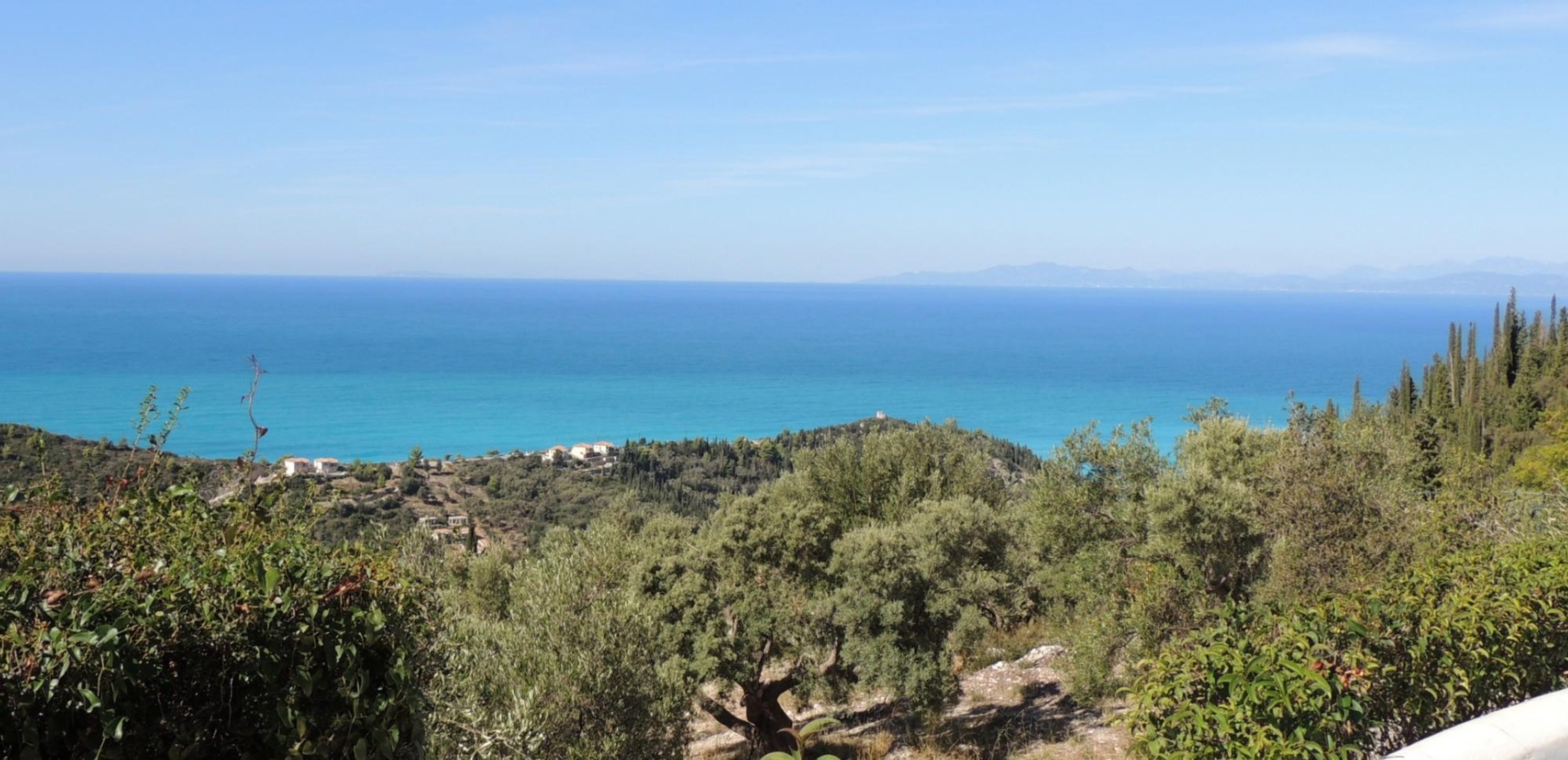 A coastal landscape with a view of the sea, vegetation, and distant mountains.