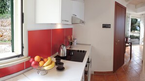 Une cuisine avec des meubles de couleur rouge, un plan de travail blanc, une machine à café et un panier de fruits.