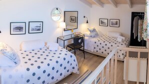 Une chambre avec deux lits, chacun recouvert d’une couvre-lit à pois, un bureau avec une lampe et des tableaux encadrés accrochés au mur.