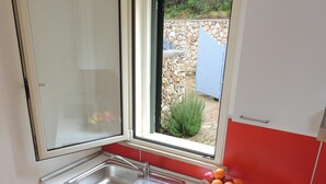 Une petite cuisine avec une fenêtre, un évier et un plan de travail sur lequel on trouve des fruits et des tasses.