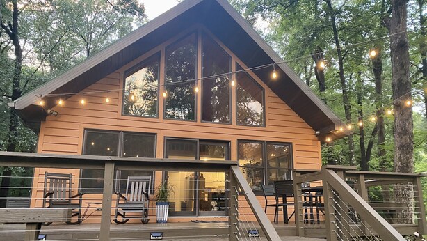 Une cabane en bois dotée de grandes fenêtres, d’une terrasse et de guirlandes lumineuses.