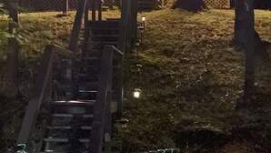 Une cabane en bois dotée de grandes fenêtres et illuminée de guirlandes lumineuses, entourée d’arbres.