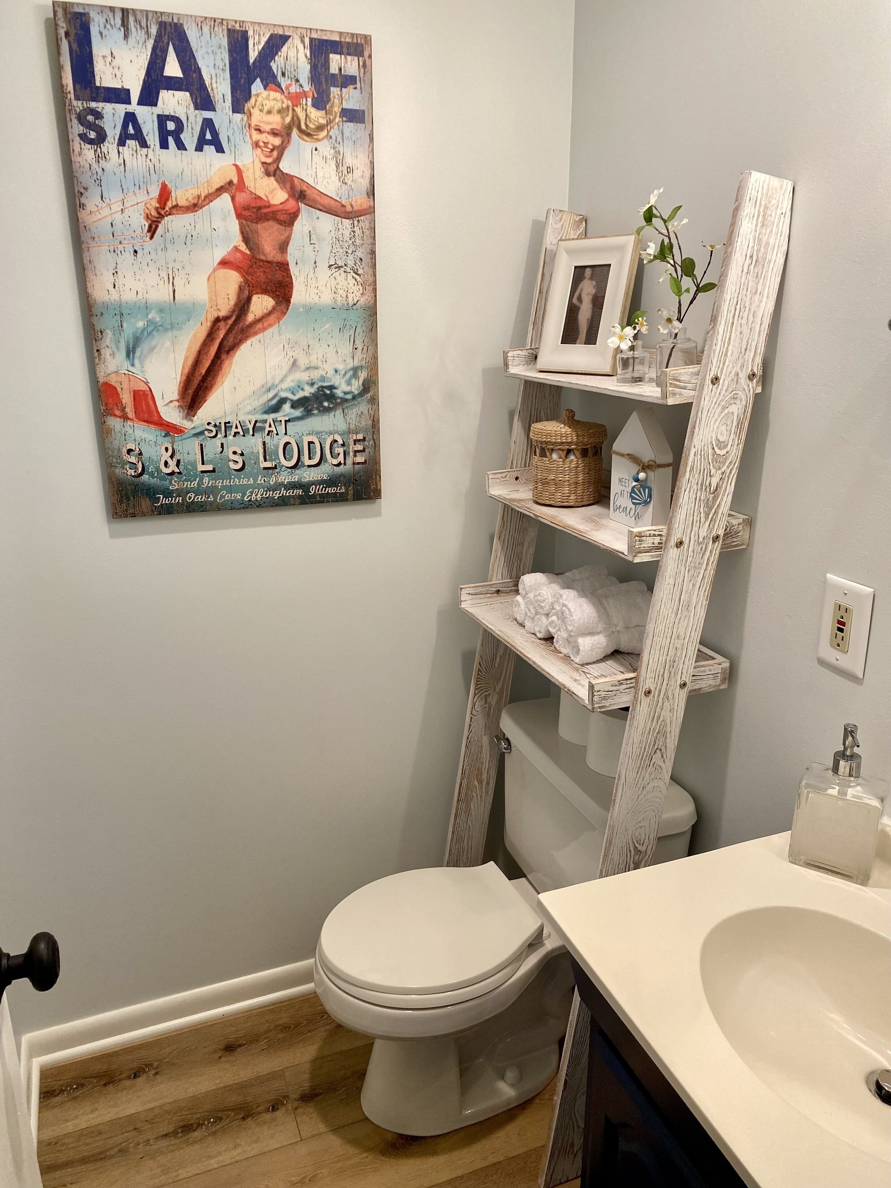 A bathroom with a white toilet, a white sink, a wooden shelf with towels, and a poster of a swimmer.