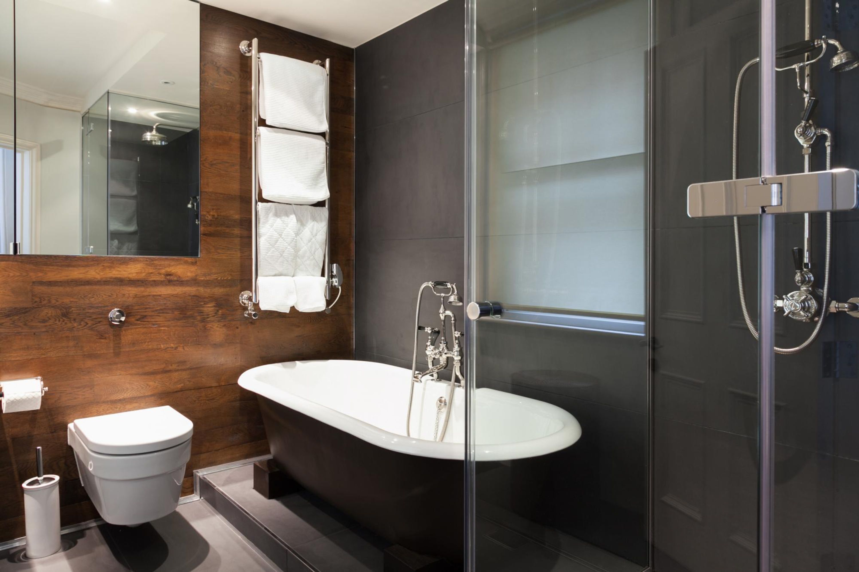 Une salle de bain moderne avec une baignoire sur pieds, une douche à parois de verre et un mur d’accent en bois.
