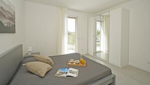 A bedroom with a bed, a bedside table with a lamp, a tray with breakfast items, and a large mirror. - Katya Resort A3 9 by Wonderful Italy (Desenzano del Garda)
