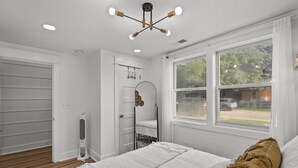 Ein Schlafzimmer mit einem großen Bett, einer Deckenleuchte, einem Fenster mit Blick nach draußen und einer Tür zu einem anderen Raum.