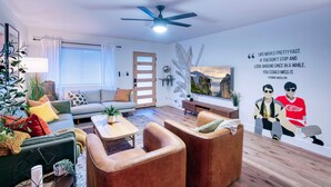 Una sala de estar moderna con un sofá, sillones, una mesa de centro y un ventilador de techo.