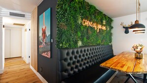 Un interior moderno con una pared verde, un letrero de neón, una mesa de comedor de madera y un banco tapizado.