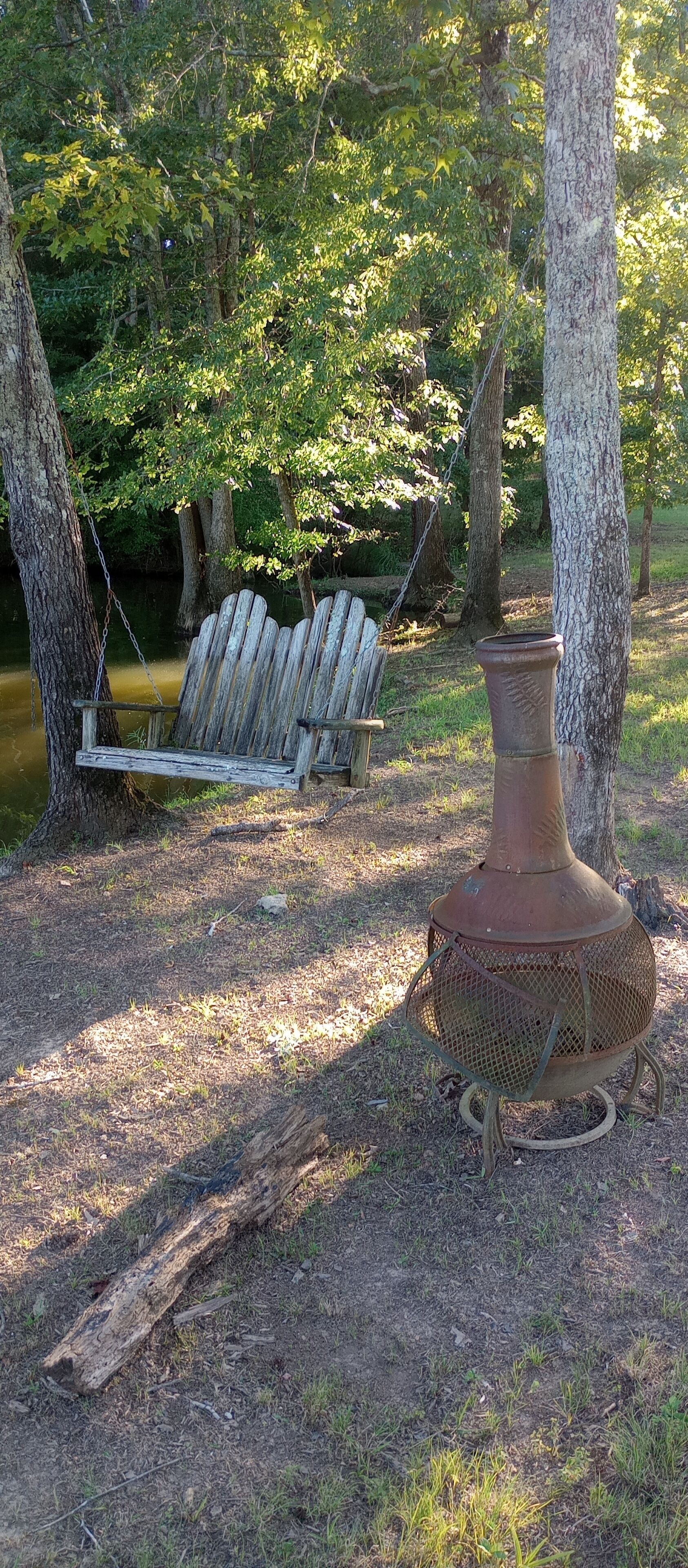 A rustic outdoor setting with a wooden swing and a metal pot.
