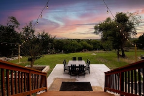 Un patio con mesa y sillas, rodeado de árboles y luces colgantes.