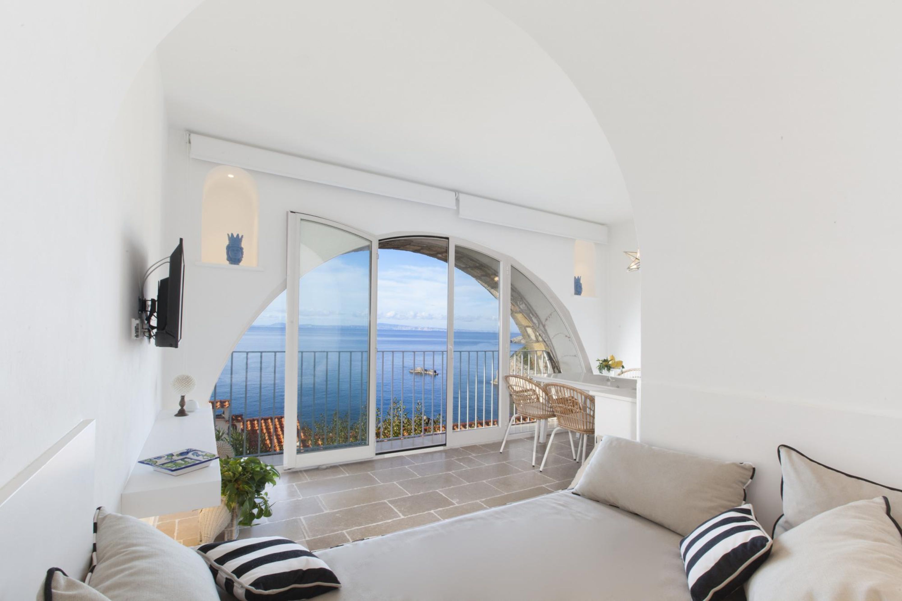 A bedroom with a large arched window, a balcony, and a view of the sea.