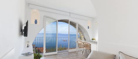 A bedroom with a large arched window, a balcony, and a view of the sea.