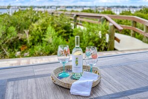 Una mesa con una botella de vino Seaglass, dos copas y una servilleta sobre un tapete tejido, con vista a un puente y follaje.