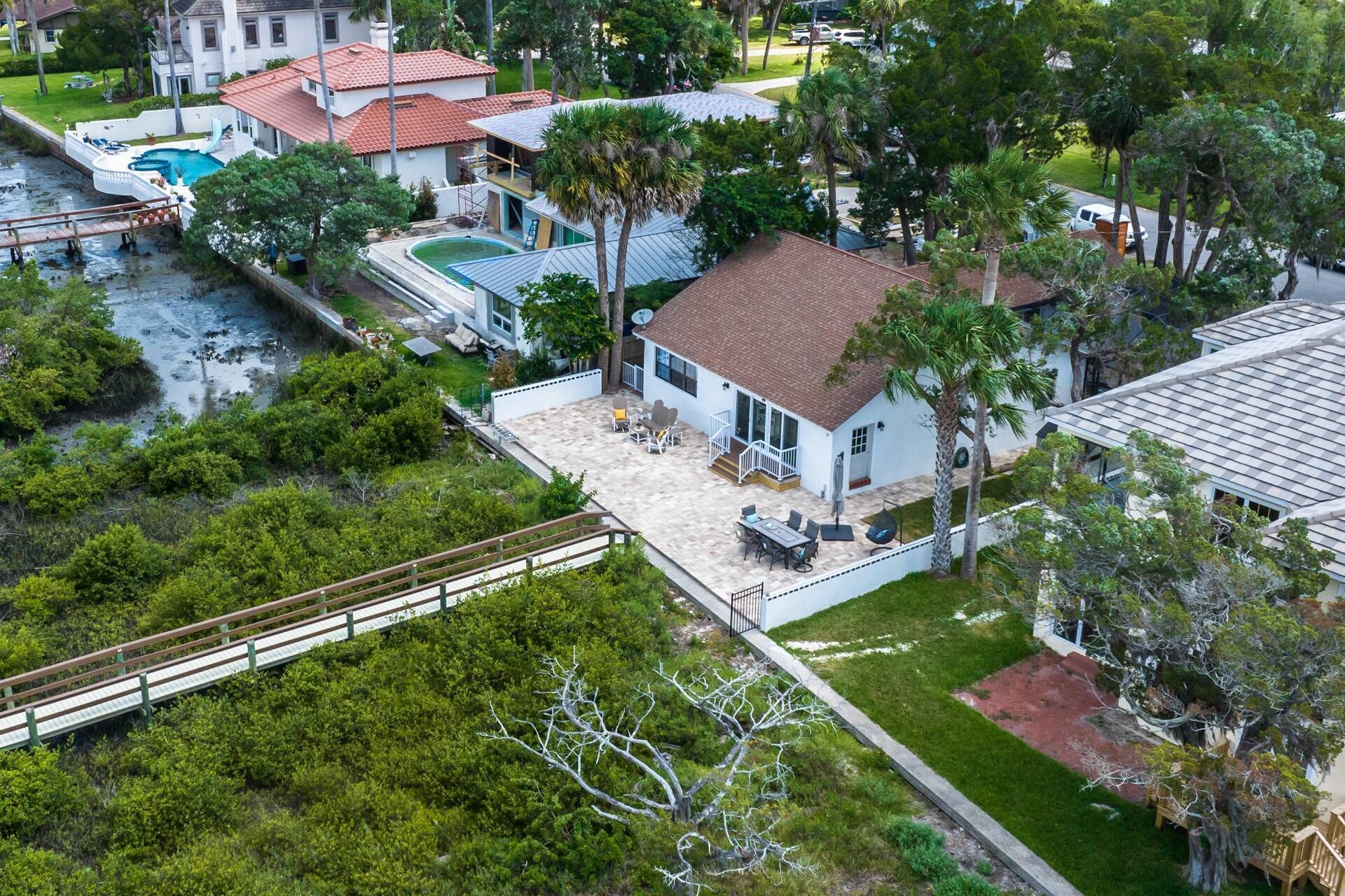 A residential area with a house featuring a patio, a swimming pool, and a bridge over a water body.