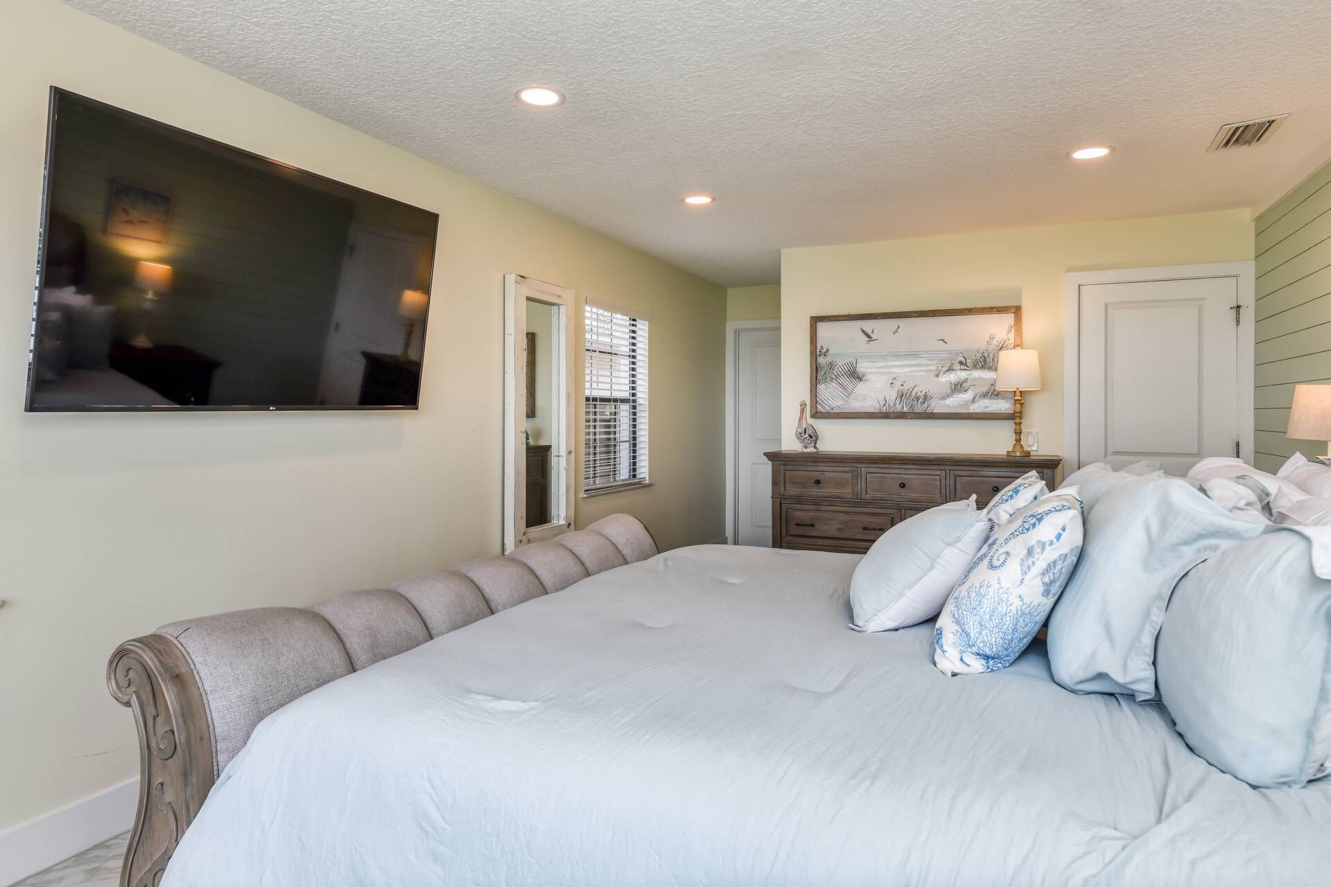 A bedroom with a large bed, a dresser, a mirror, and a painting on the wall.