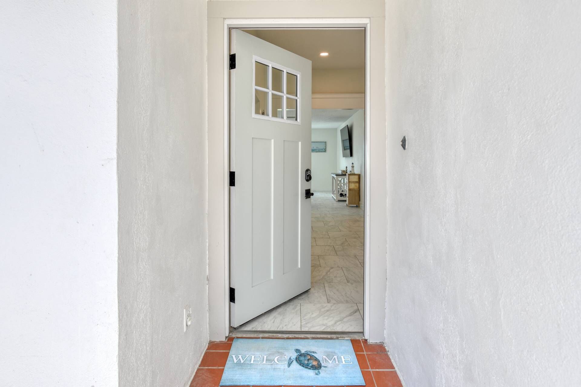 A hallway with a white door, a welcome mat with a turtle design, and a tiled floor.