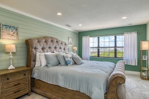 Un dormitorio con una cama grande, mesitas de noche de madera, un ventanal con cortinas y vistas al exterior.