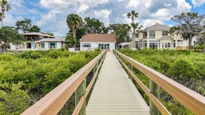 A wooden boardwalk leading to a white building with a red roof, surrounded by lush greenery and palm trees. - Dolphin View (St. Augustine)