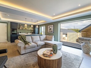 Una sala de estar moderna con un sofá seccional gris, una mesa de centro redonda con libros y vistas al patio trasero.