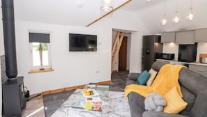 A modern living room with a sofa, a coffee table, a TV, and a kitchen area in the background. - Lands Brow Lodge (Wigton)