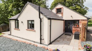 A two-story house with a tiled driveway, a small front porch, and a stone wall. - Lands Brow Lodge (Wigton)