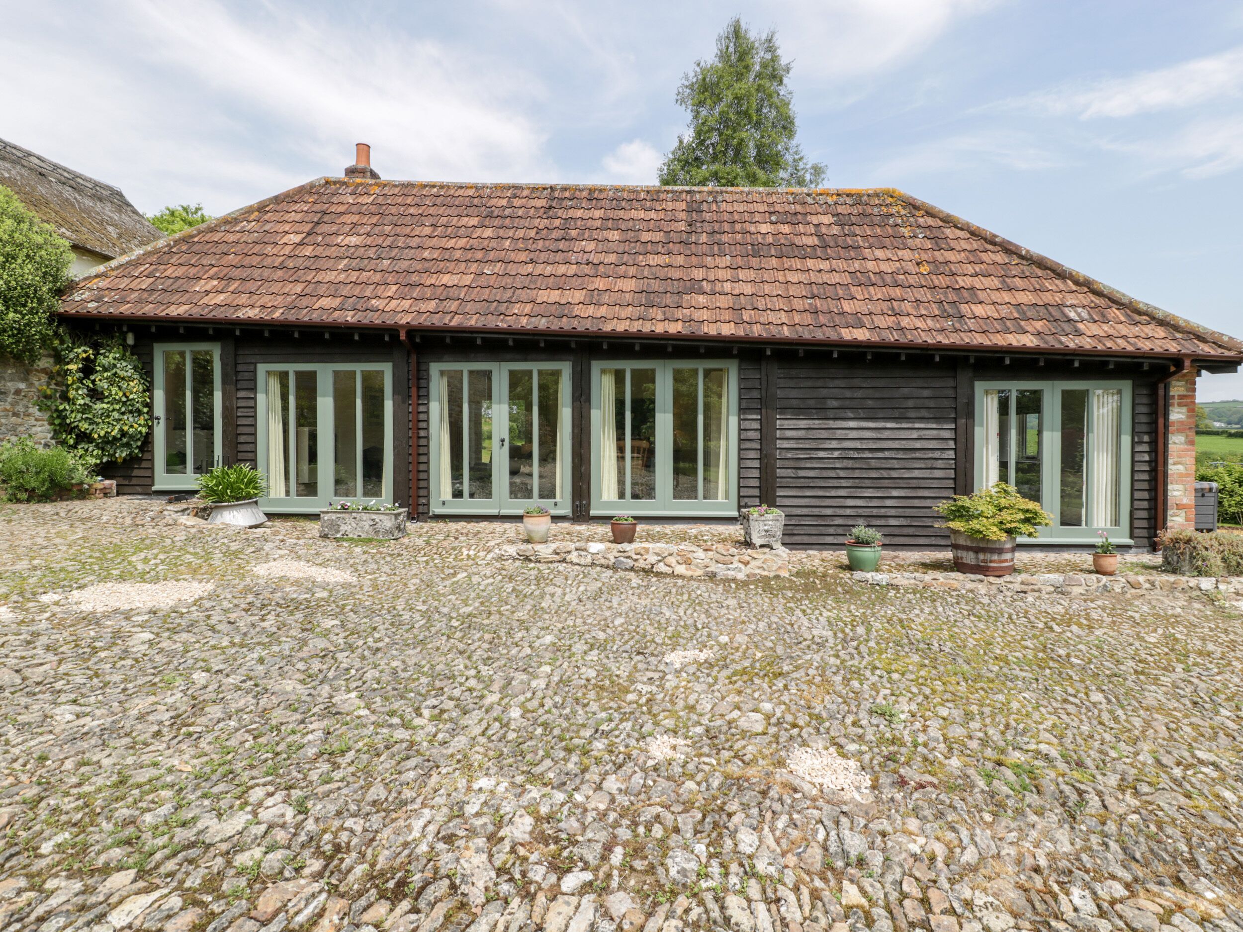 A rustic building with a tiled roof, large windows, and a stone-paved ground.