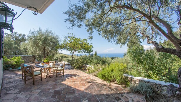 Eine Terrasse im Freien mit Tisch und Stühlen, umgeben von Steinmauern und Vegetation, mit Blick auf eine reizvolle Landschaft.