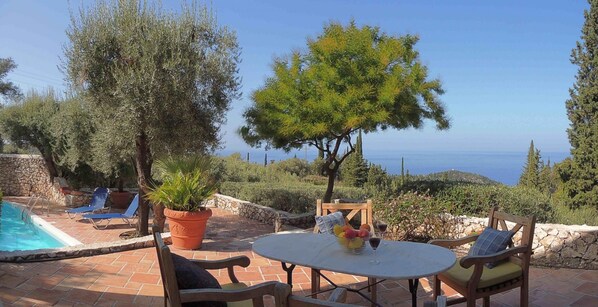 A pool area with lounge chairs, a table with fruit and drinks, and a view of the sea. - Villa Mimosa - Agios Nikitas Villas (Lefkada)