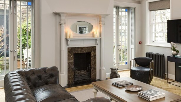 A spacious living room with a leather sofa, a fireplace, and a television. - The Park Lane Penthouse (London)