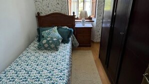 Un dormitorio con cama, mesita de noche, cómoda, ventana con cortinas y puerta.