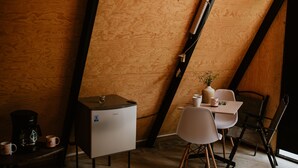 Una habitación acogedora con techo de madera inclinado, una pequeña kitchenette, una mesa de comedor con sillas y una cafetera.